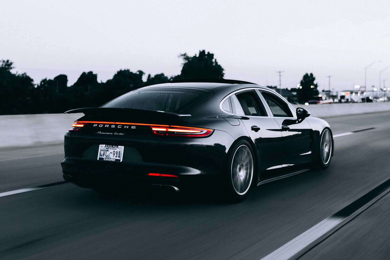 Black Porsche driving at dusk, rear three-quarter view