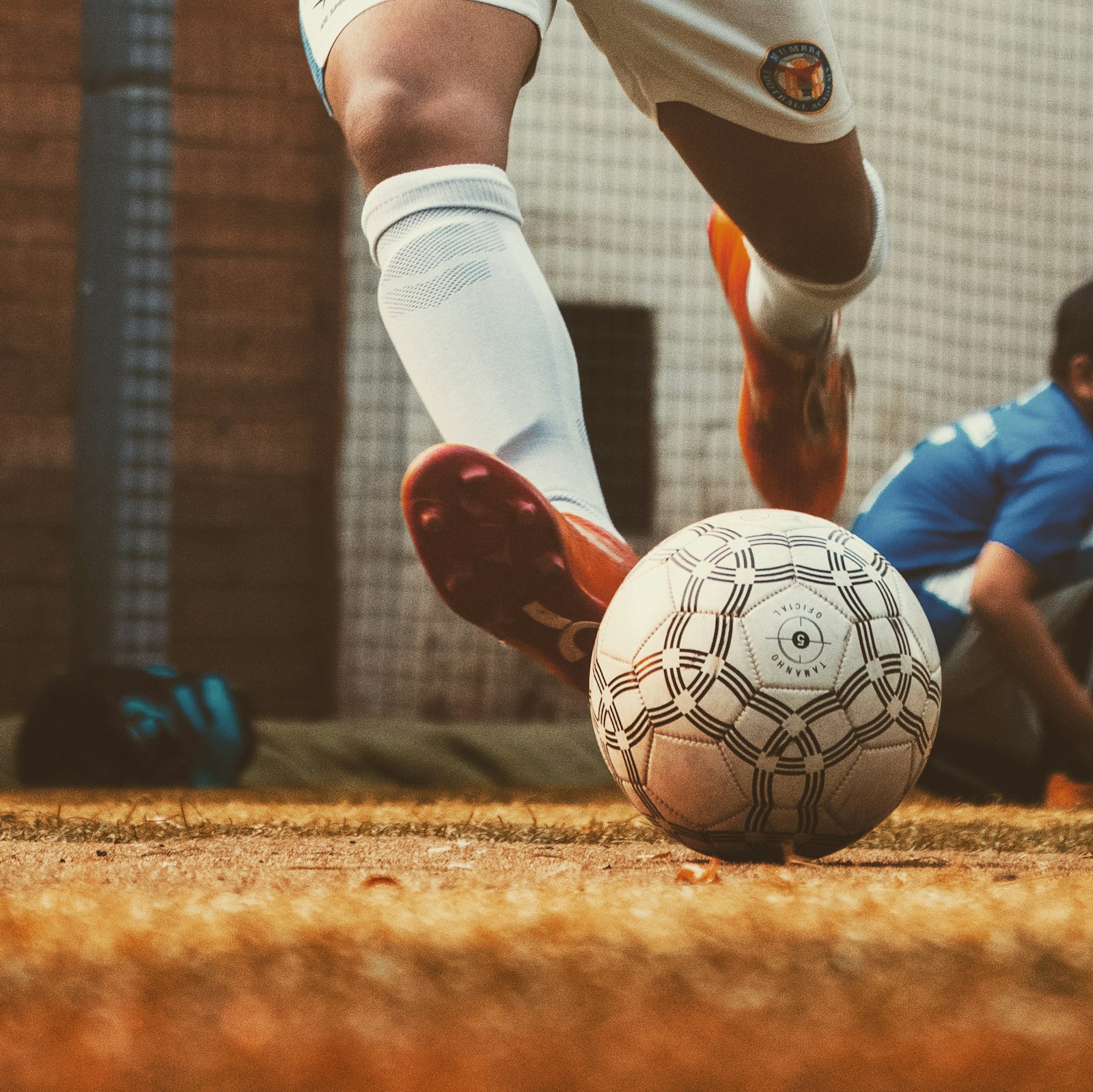 Low-angle shot of a soccer player striking the ball on a dusty pitch